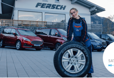 KFZ Mechatronikerin Tanja Kennerknecht steht hinter Autoreifen vor dem Gebäude des Autohaus Fersch